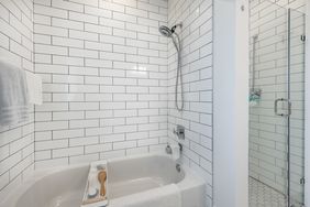 Bathroom with white tiled walls a bathtub with a wooden tray and a glass shower enclosure