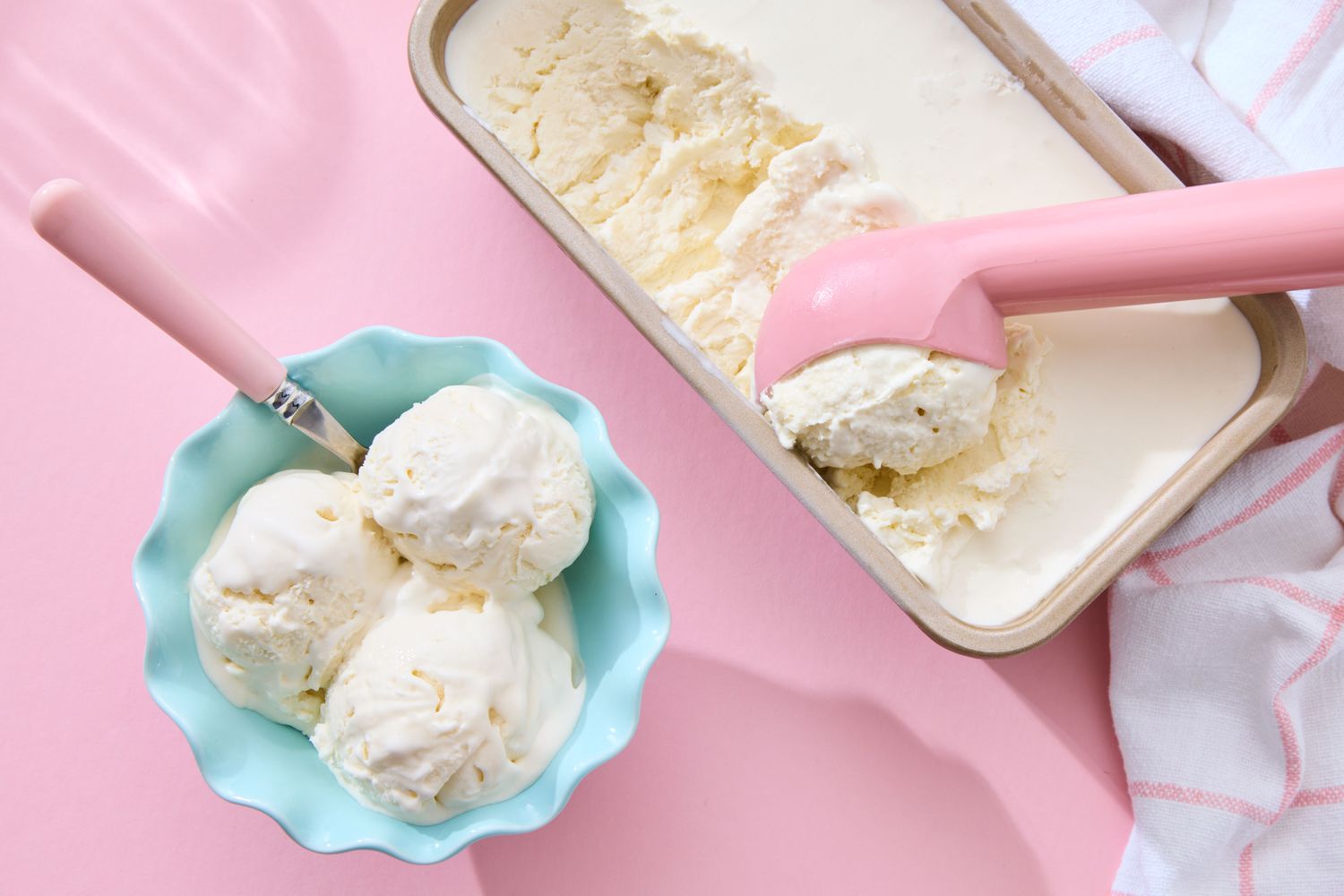 A bowl of scooped vanilla ice cream next to a tub with an ice cream scooper