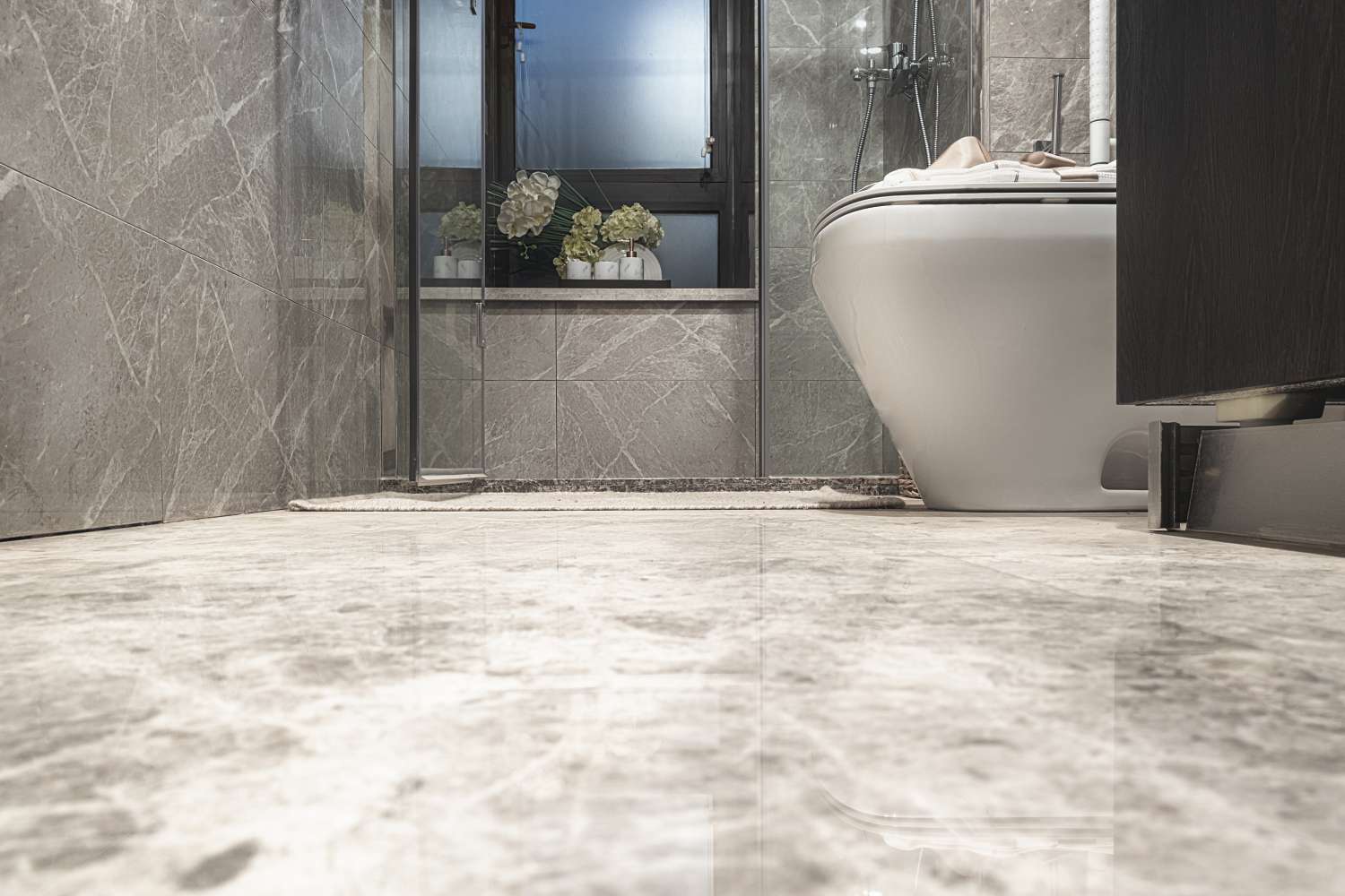 Modern bathroom with a tiled floor a white toilet a glass shower door and a view of a window with potted plants