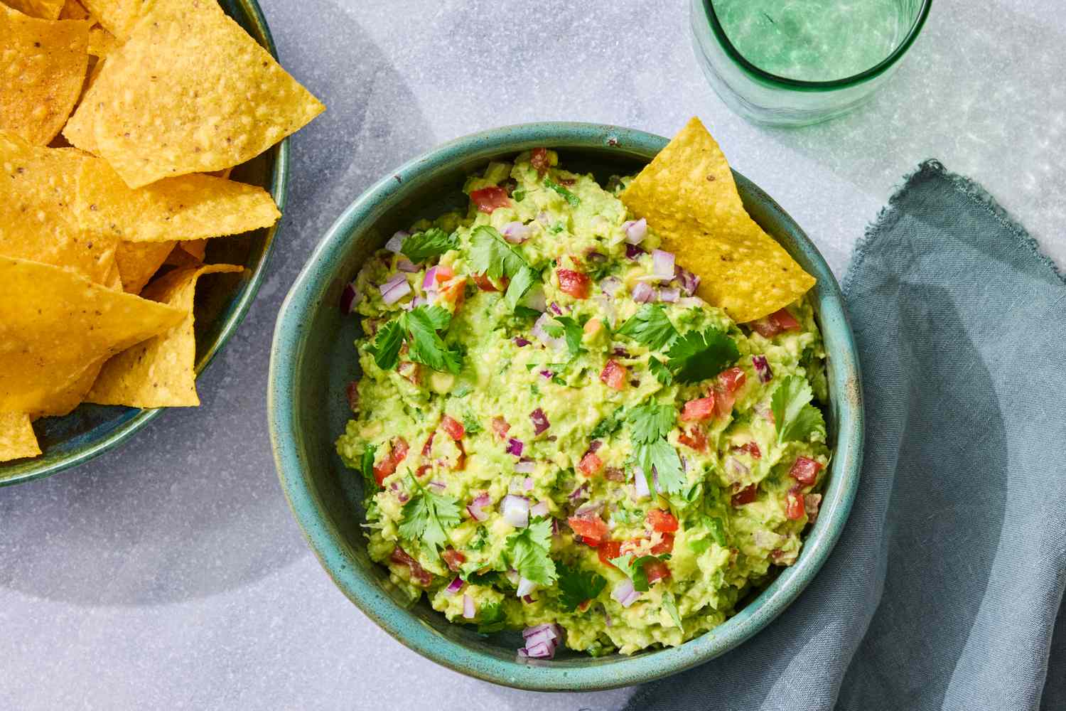 Bowl of guacamole garnished with diced vegetables and cilantro served with tortilla chips on a table