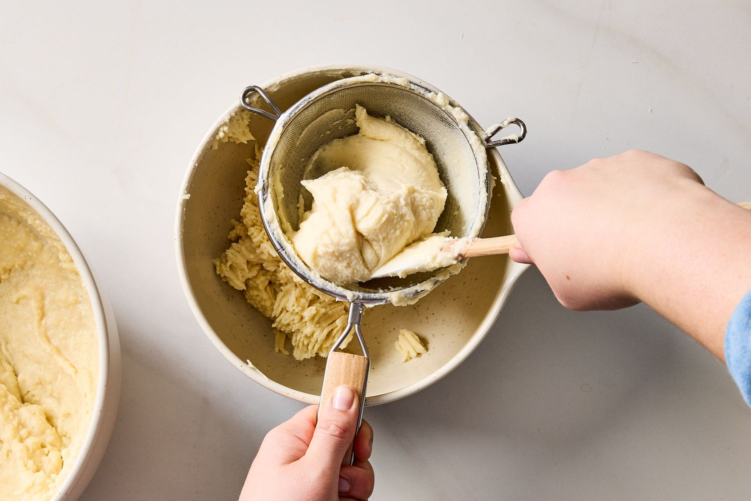 Hands straining potato puree into a bowl