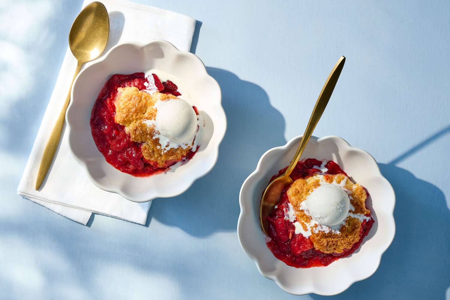 Two bowls of strawberry cobbler topped with scoops of ice cream, accompanied by golden spoons