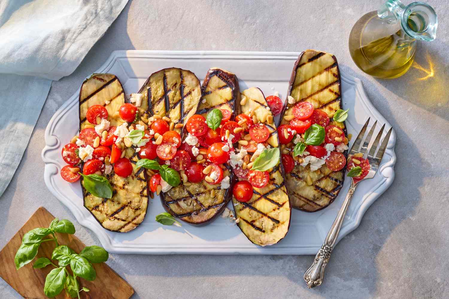 Grilled eggplant slices topped with diced tomatoes, feta cheese, and basil, served on a white platter