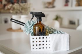 A cleaning spray bottle and a microfiber duster in a basket