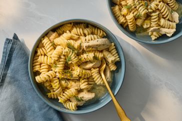 A bowl of pasta with chicken and herbs served with a fork