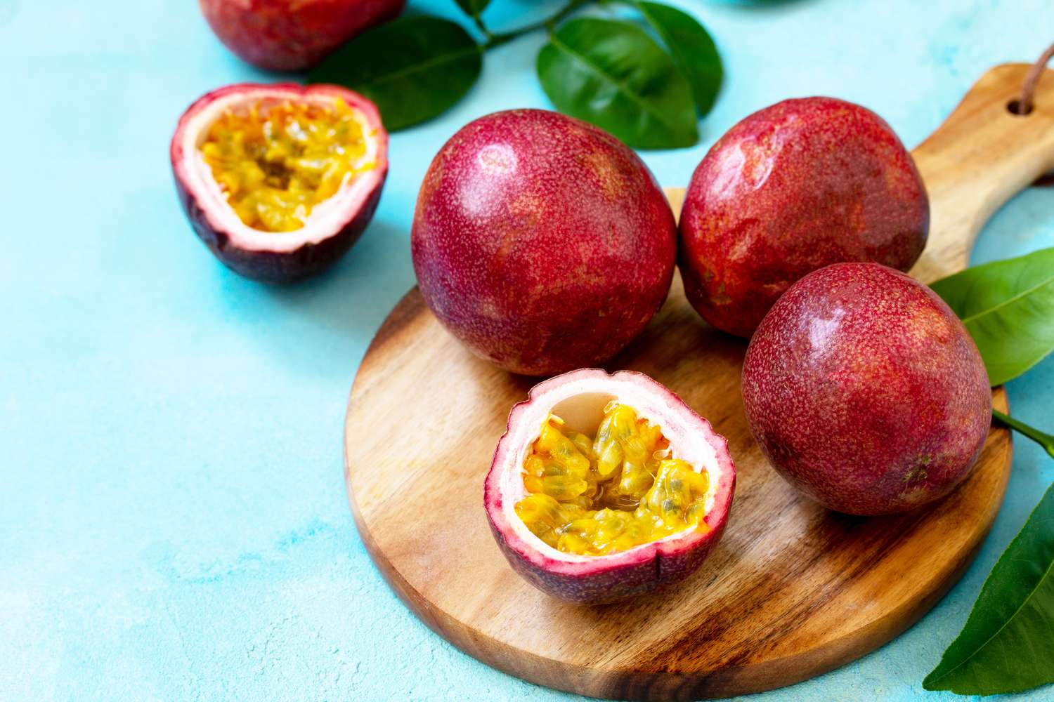 passion fruit halves and whole fruit on wooden board on blue surface