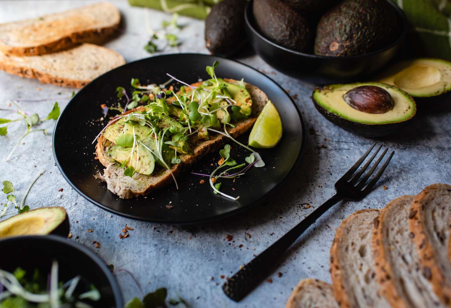 Avocado toast on a plate with ingredients around it on stone counter.