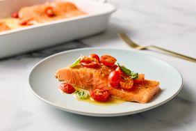 A plate with a portion of baked salmon garnished with cherry tomatoes and herbs a baking dish in the background