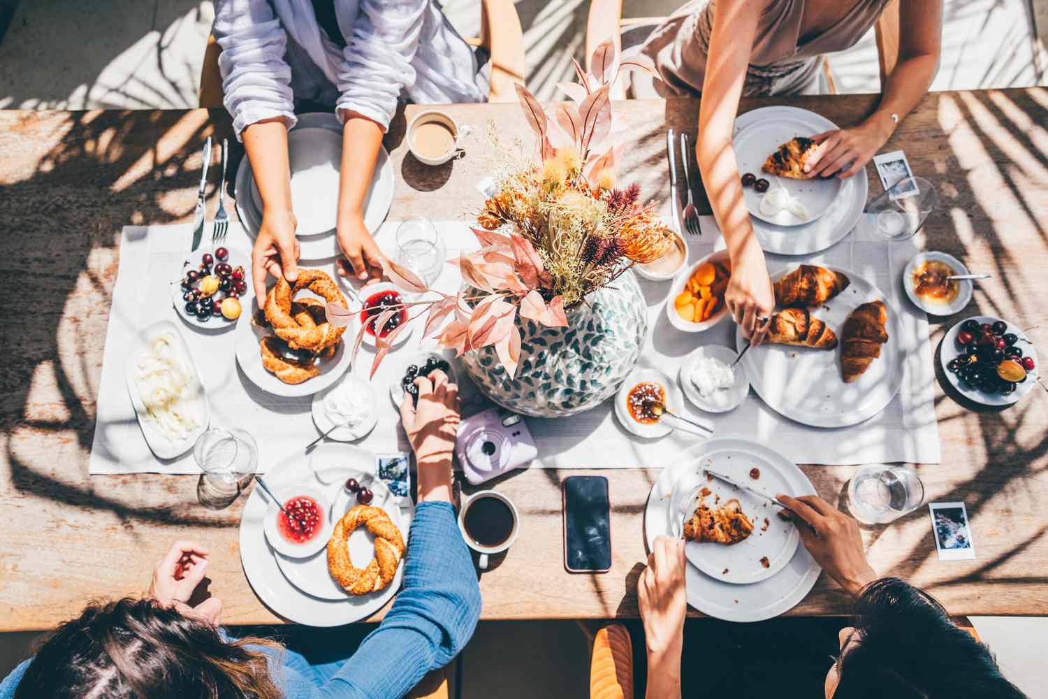 People enjoying food at a dining table with pastries, fruit, and coffee