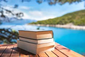 Stack of books on an outdoor table with a blurred lake view in the background