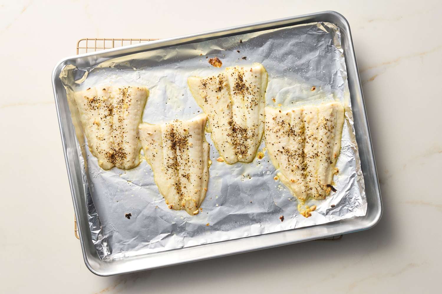 Broiled fish fillets on a baking sheet lined with aluminum foil