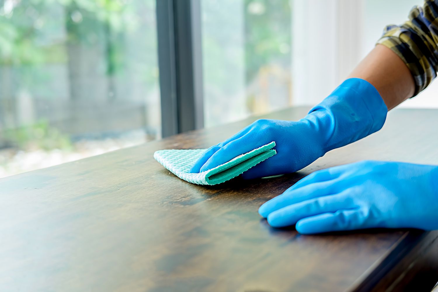 Person wearing blue gloves dusting wooden table