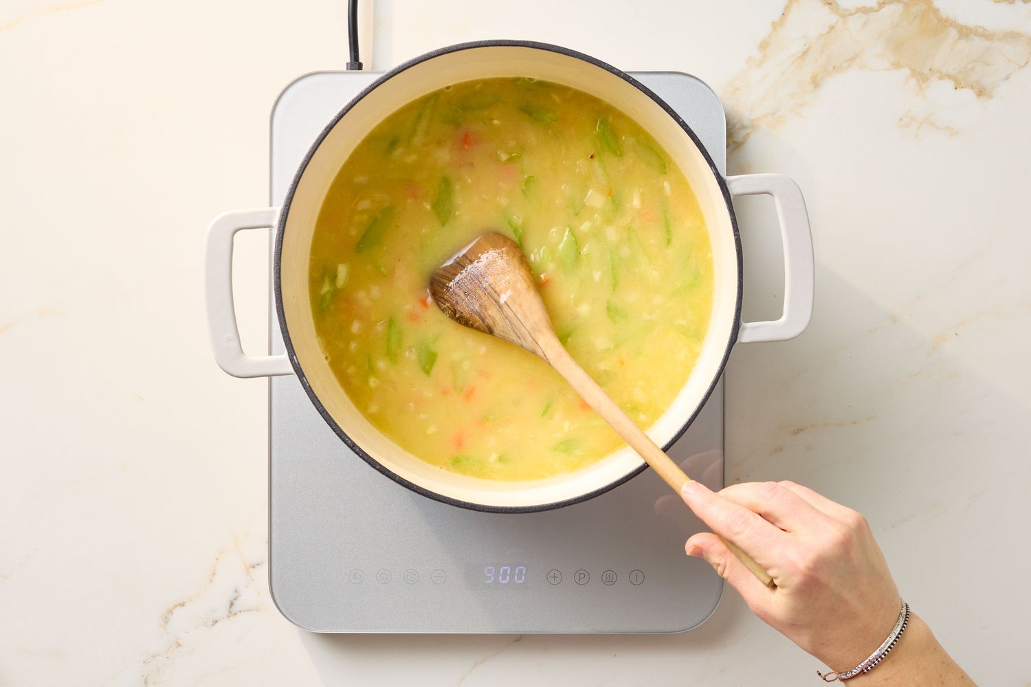 A pot of chicken and dumplings being stirred with a wooden spoon on an induction cooktop