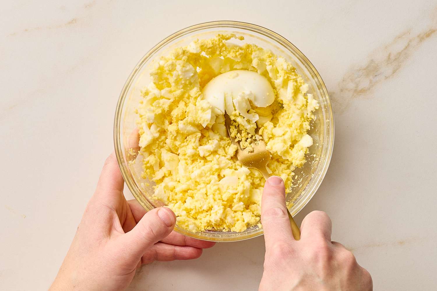 Hands mashing ingredients in a bowl including hardboiled eggs