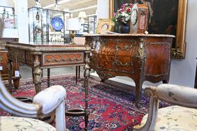 An antique furniture display including a table a dresser and a redpatterned carpet in an antique shop setting