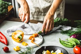 Close-up of woman chopping vegetable on kitchen counter. Hands of female chopping carrot and bell pepper on cutting board.