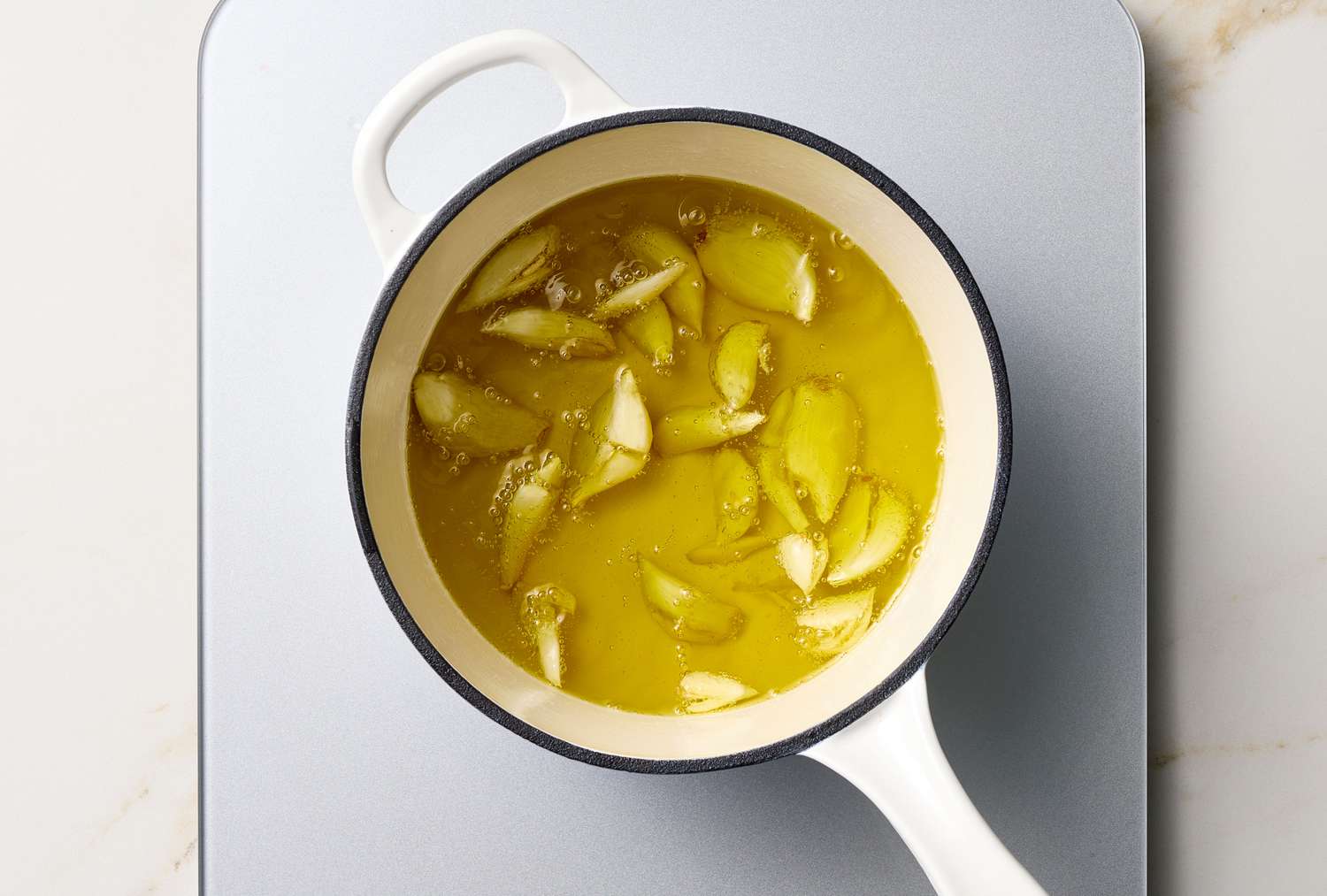 A pot containing oil and garlic slices on a stovetop