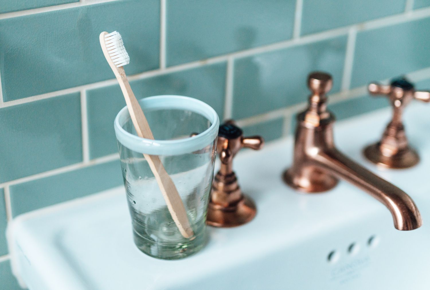 A toothbrush in a glass cup on a bathroom sink beside a faucet