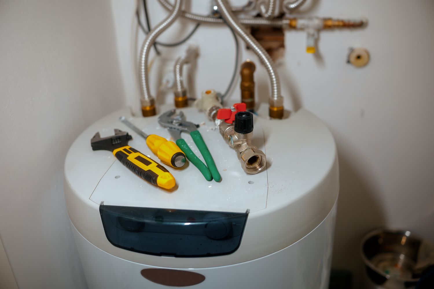 A water heater with various tools placed on it including wrenches and screwdrivers indicating maintenance or repair work