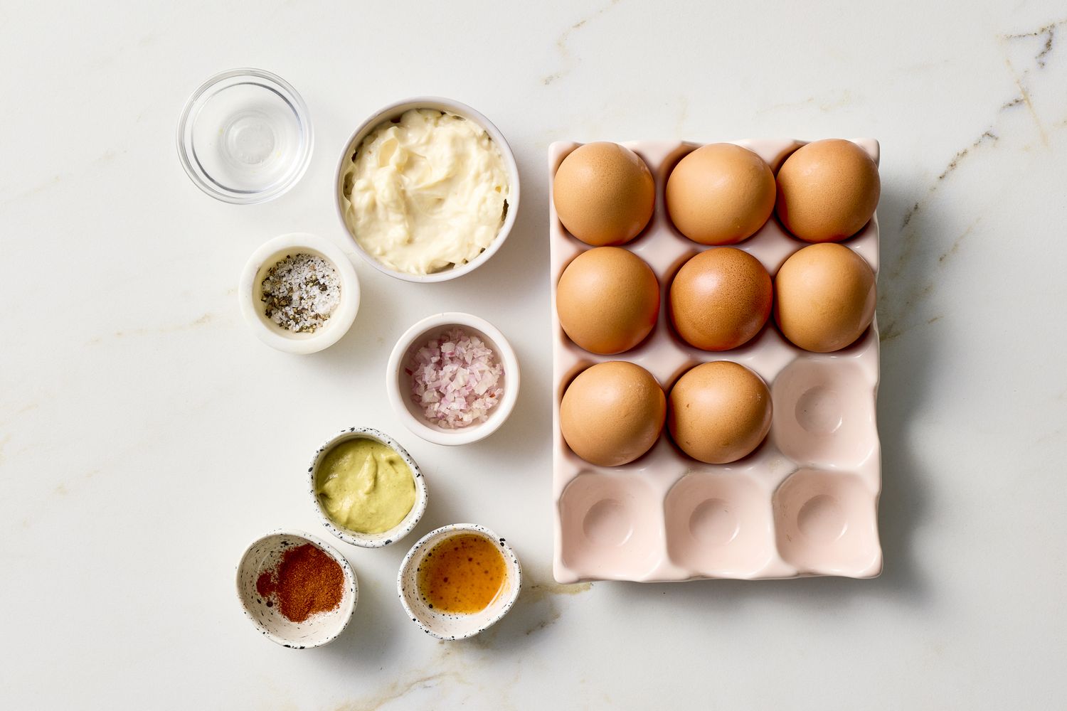 Ingredients for making deviled eggs arranged on a countertop including eggs seasonings and mayonnaise
