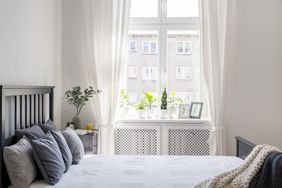 A bedroom with a bed next to a window adorned with plants and framed pictures on the sill