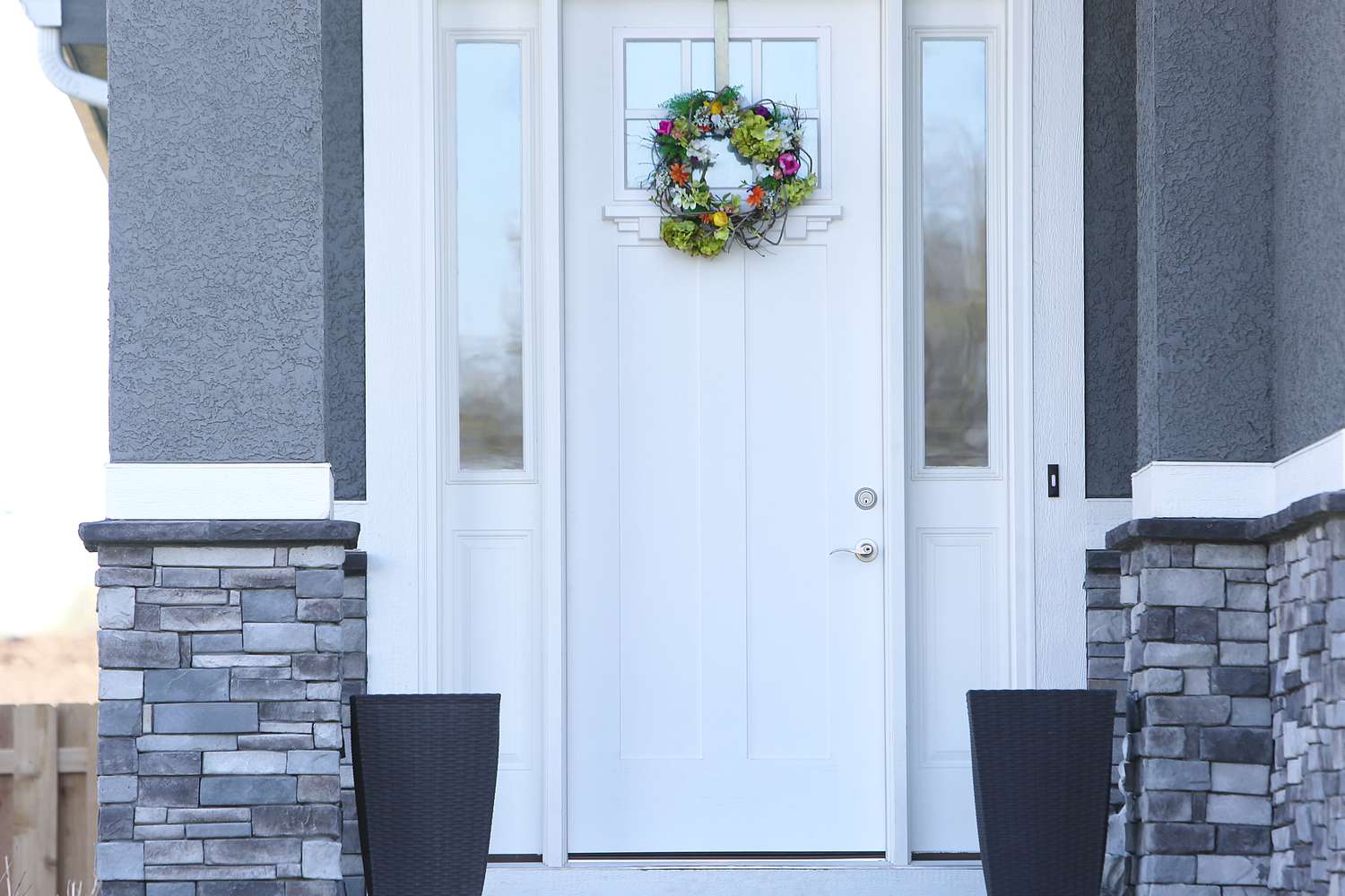 Front door of a modern home with a decorative wreath and two planters