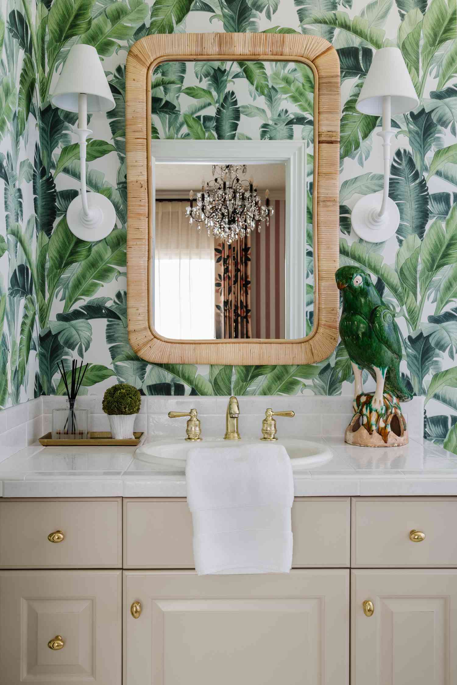 a bamboo mirror and plaster sconces against a leafy green wallpaper