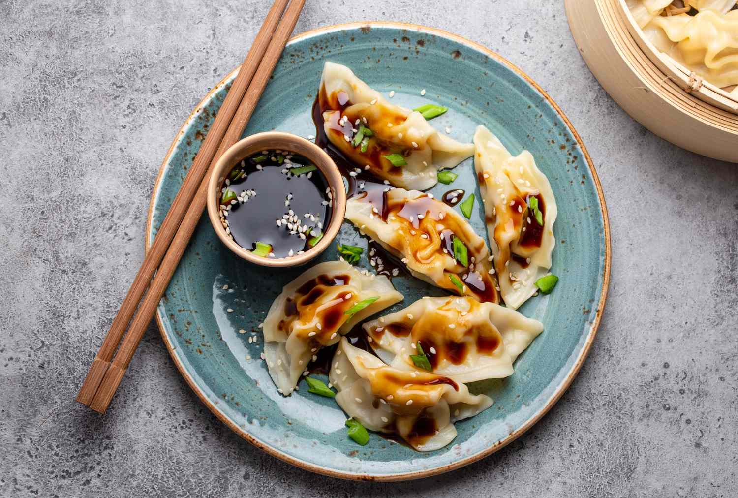 A plate of dumplings with dipping sauce and chopsticks