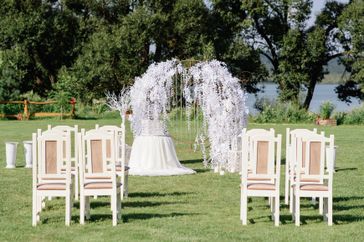 Outdoor wedding ceremony setup with chairs and a floral arch on a grassy lawn near a lake