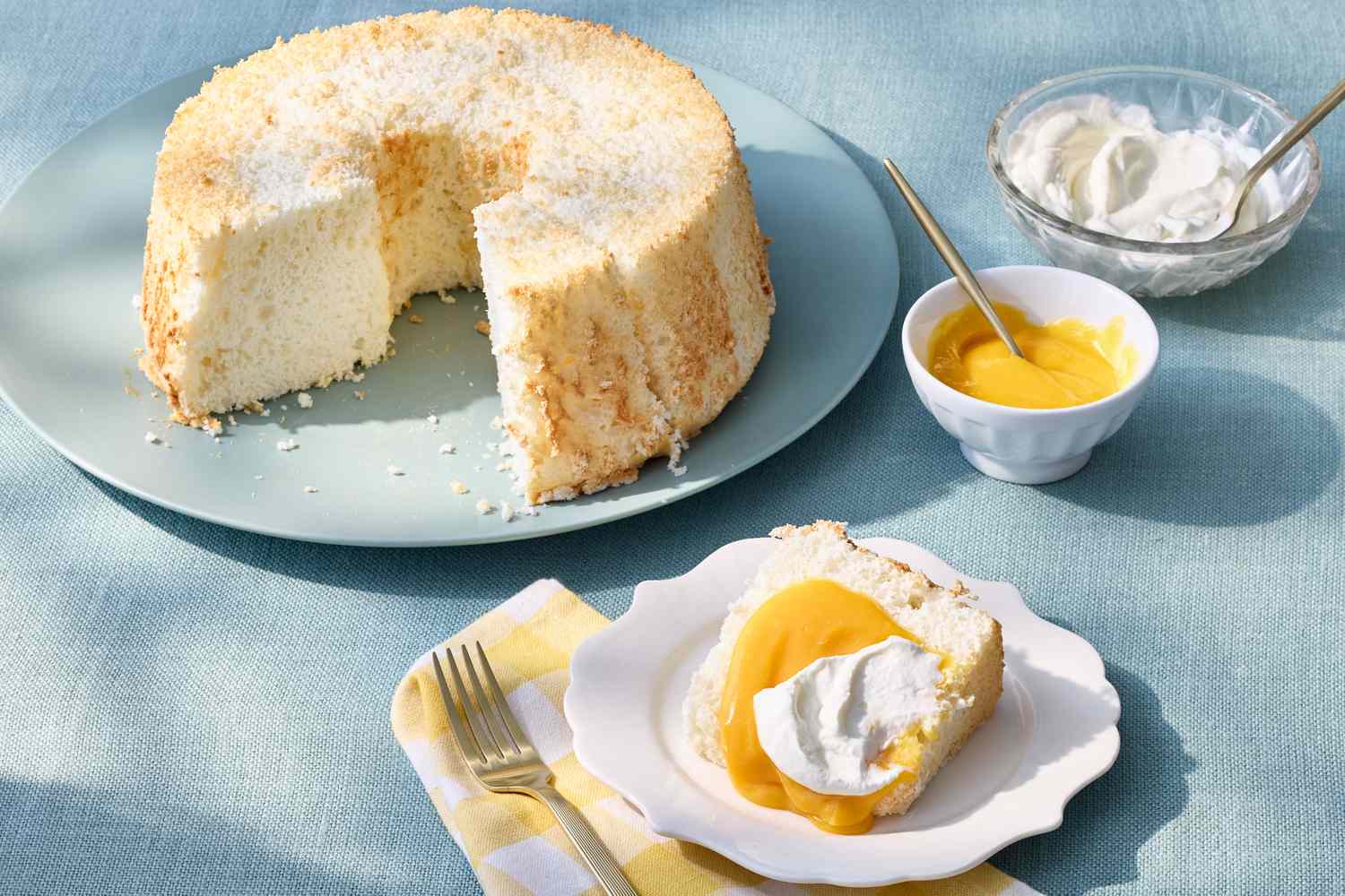 Angel food cake with a slice served, topped with whipped cream and a yellow sauce