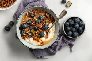 A bowl of yogurt with granola blueberries and a spoon next to a dish of blueberries
