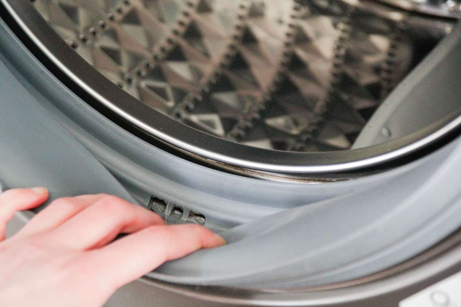 A persons hand inspecting the rubber seal of a washing machine drum