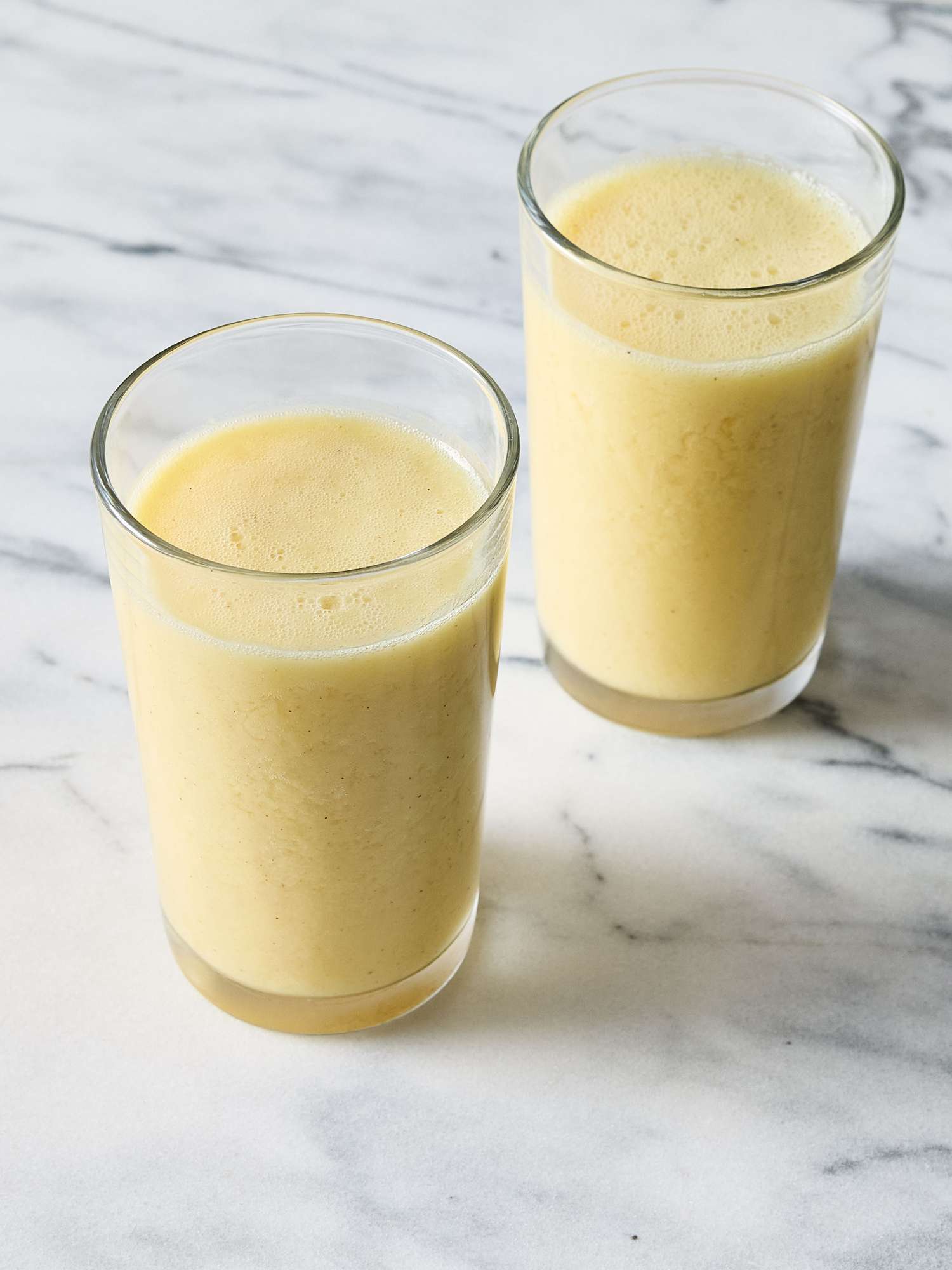Two glasses of pineapple and ginger smoothie on a marble surface