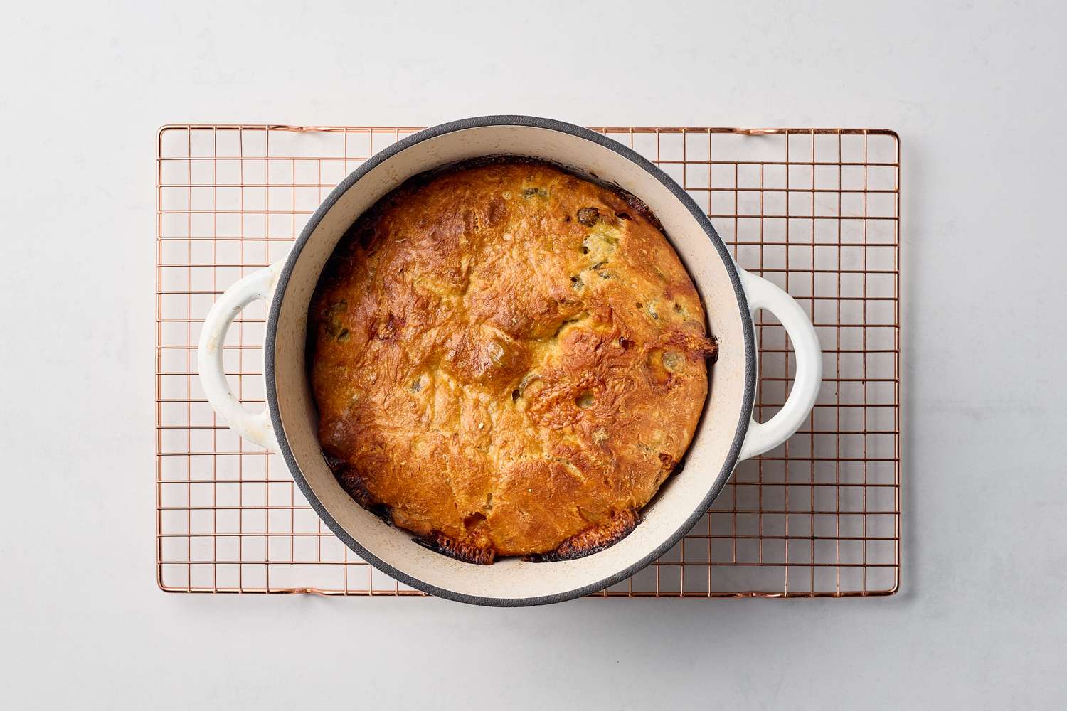 A baked loaf with olives and cheese in a round dish on a cooling rack