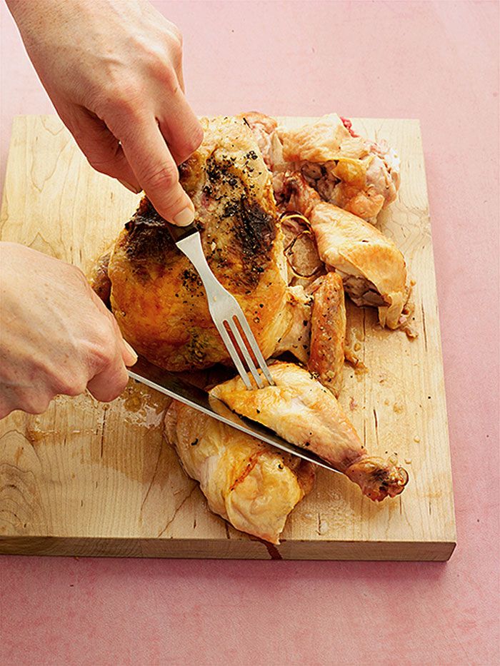 Carving a roasted chicken on a wooden cutting board with a knife and fork