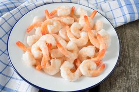 A plate of cooked shrimp with tails arranged on a white dish on a surface with a checkered cloth