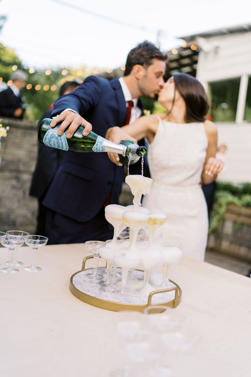 bride and groom share a kiss while pouring champagne on glass tower