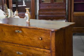 A wooden dresser with a decorative vase placed on top visible in a room with other wooden furniture
