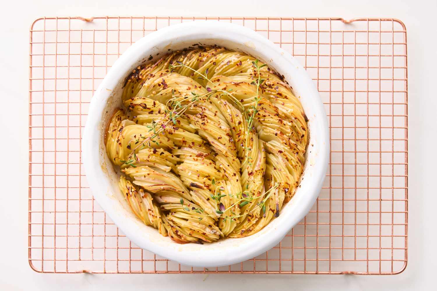 A crispy potato roast with herbs in a round white dish on a cooling rack