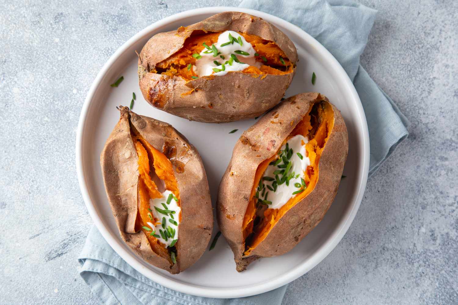 Plate with three baked sweet potatoes topped with sour cream and chopped chives placed on a light cloth