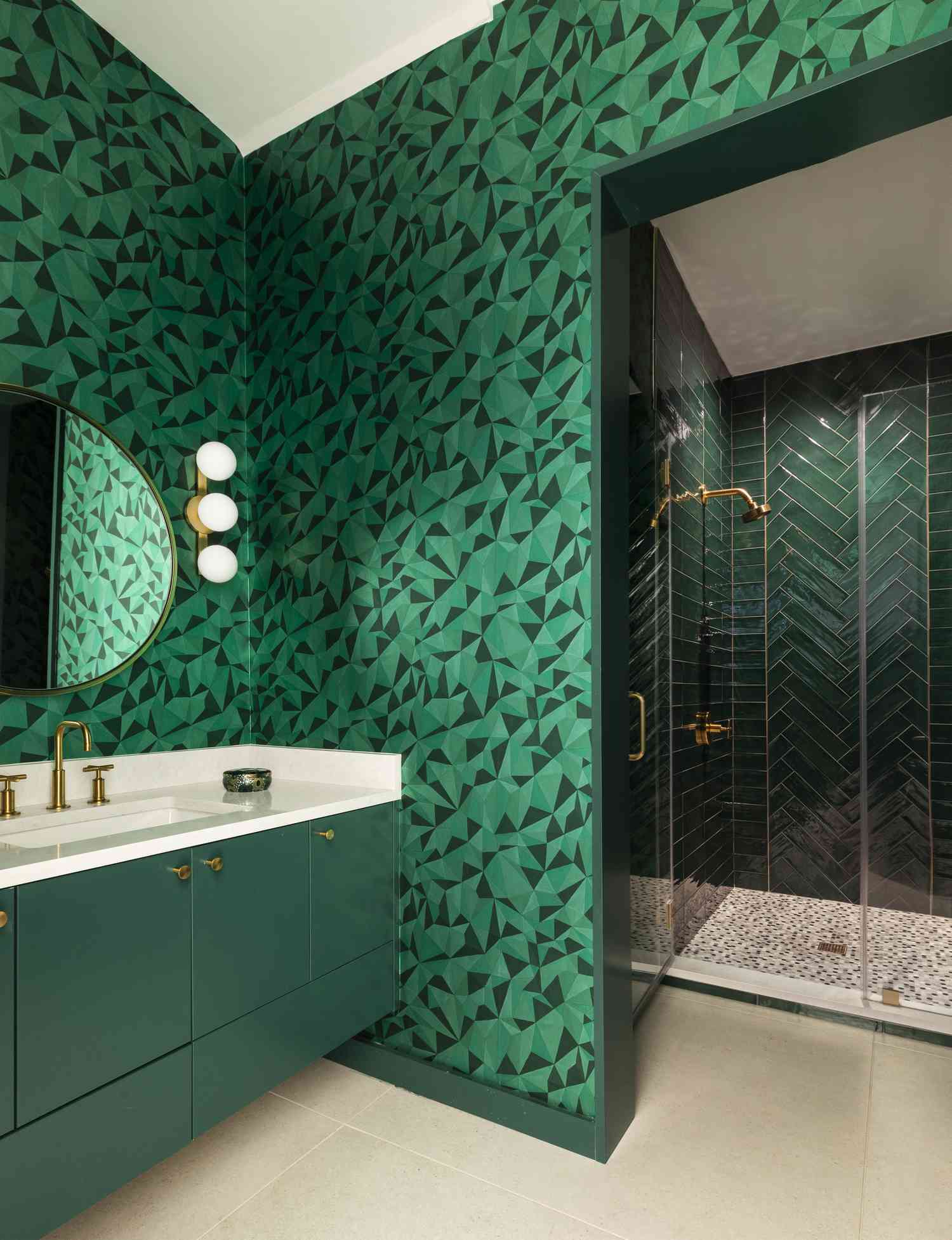 A geometric wallpapered bathroom with green lacquer cabinets and emerald tiled shower