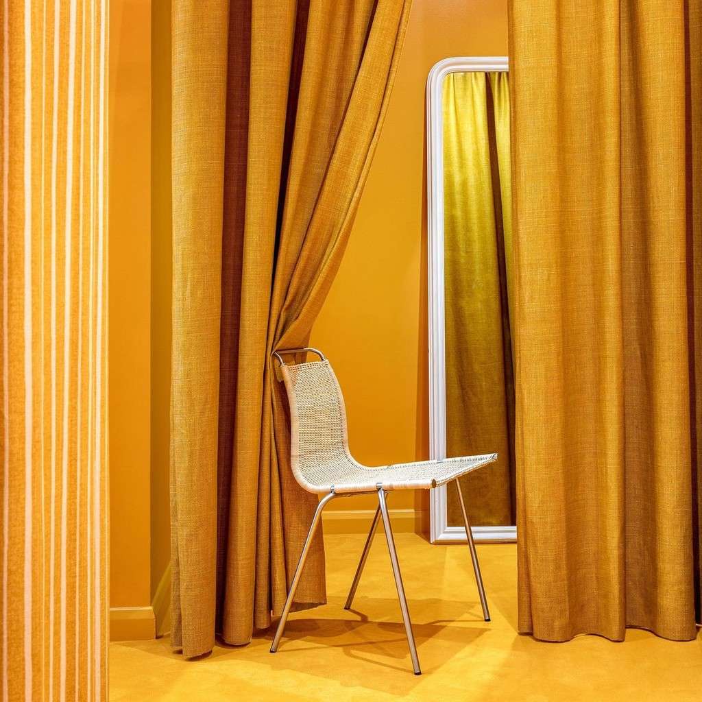 A white chair inside a room with curtains and a mirror