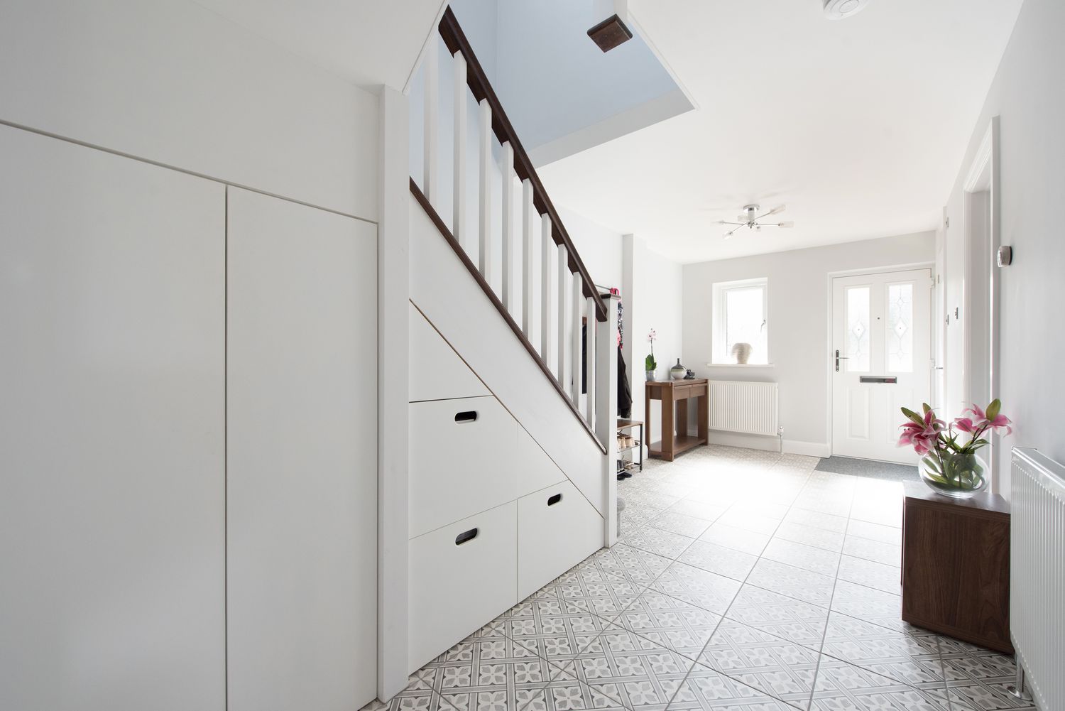 A general view of a hall with patterned tiled floor and built in under stairs storage within a home