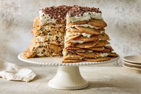 A layered chocolate chip cookie icebox cake on a ceramic stand with a slice taken out to show the layers