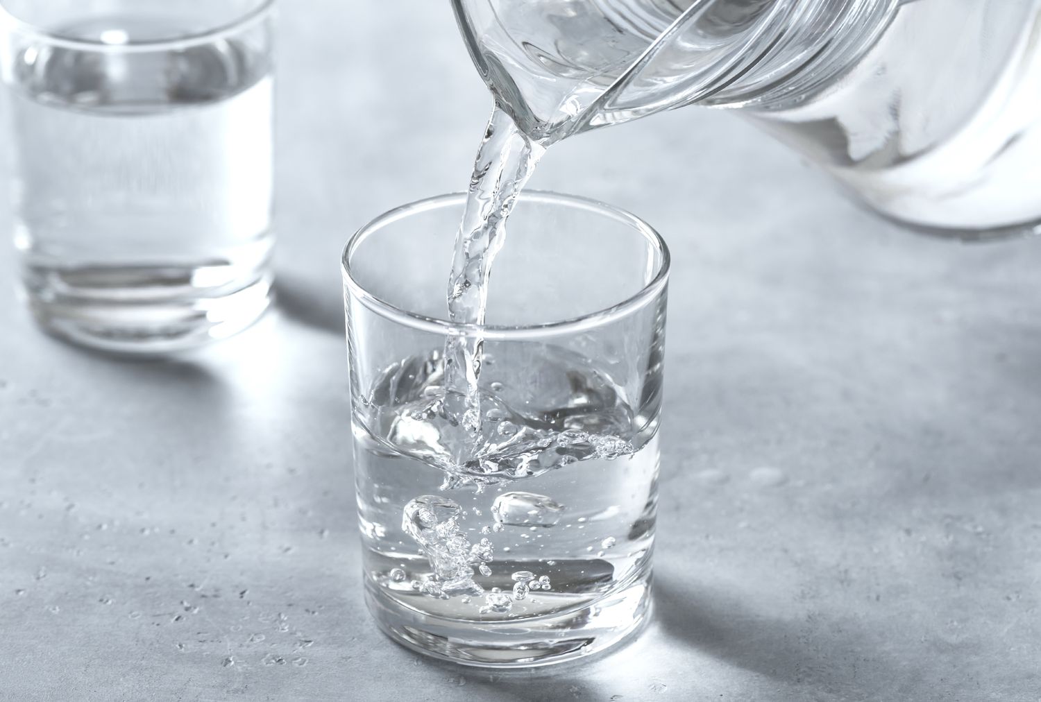 Water being poured from a pitcher into a glass with a second glass filled in the background
