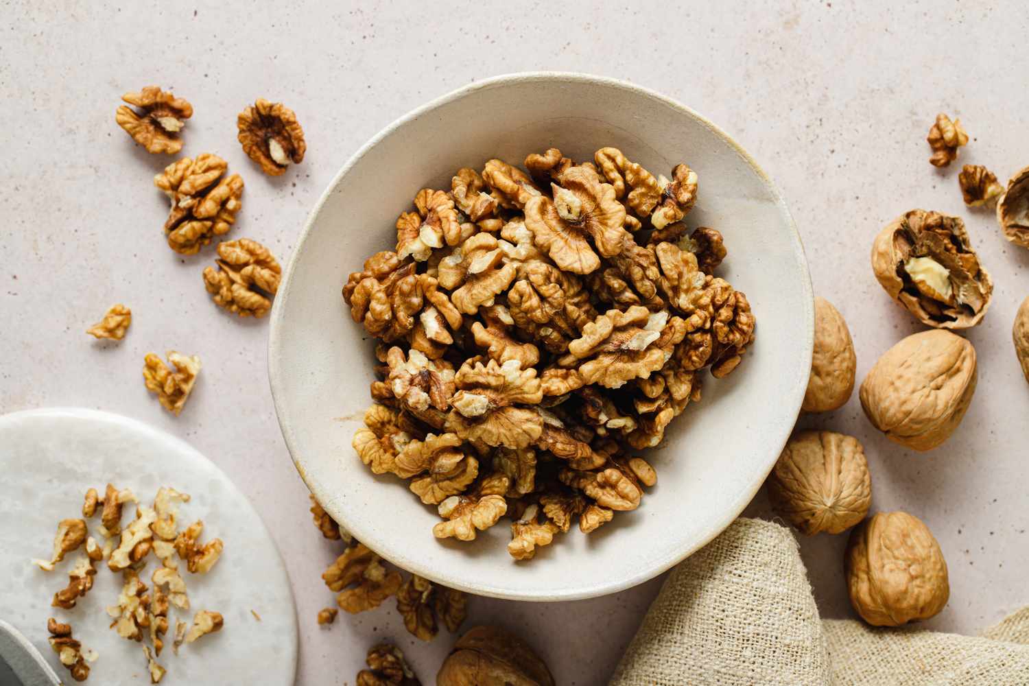 bowl of shelled walnuts on white table with shelled and unshelled walnuts