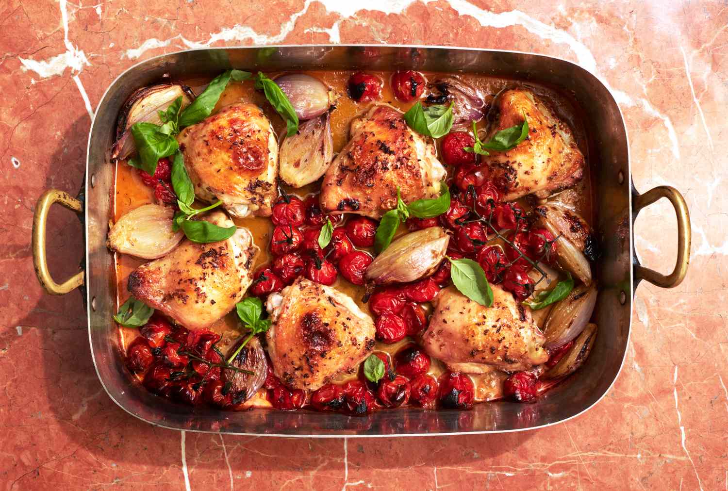 Baked chicken thighs with roasted cherry tomatoes shallots and basil in a roasting pan
