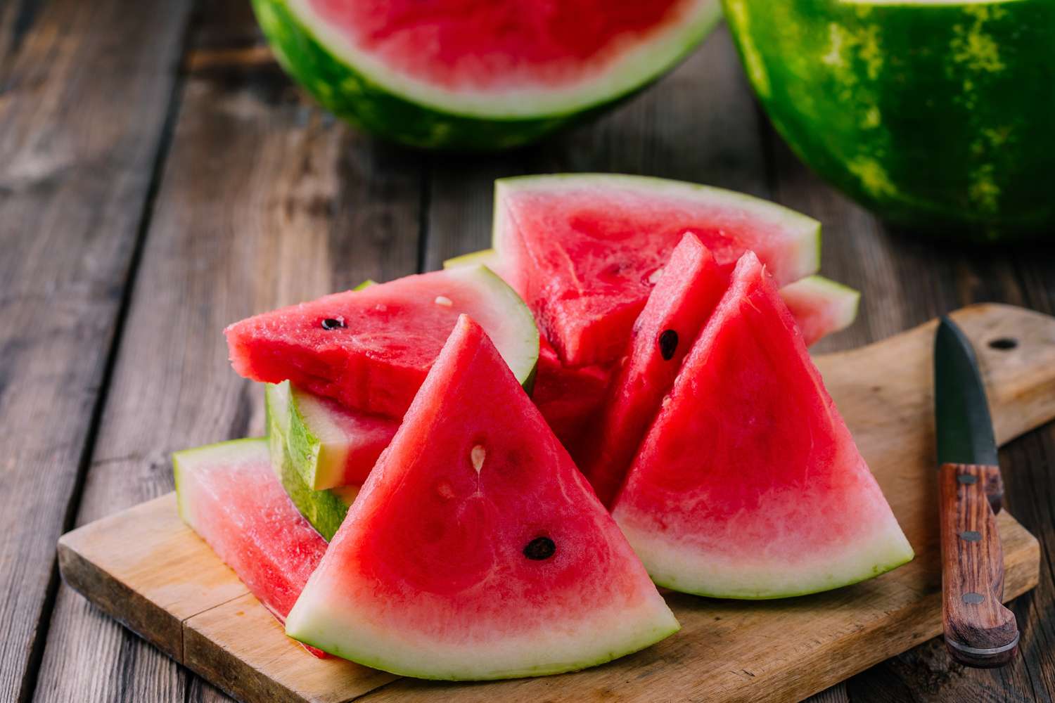 Slices of watermelon on a wooden cutting board with a knife beside them