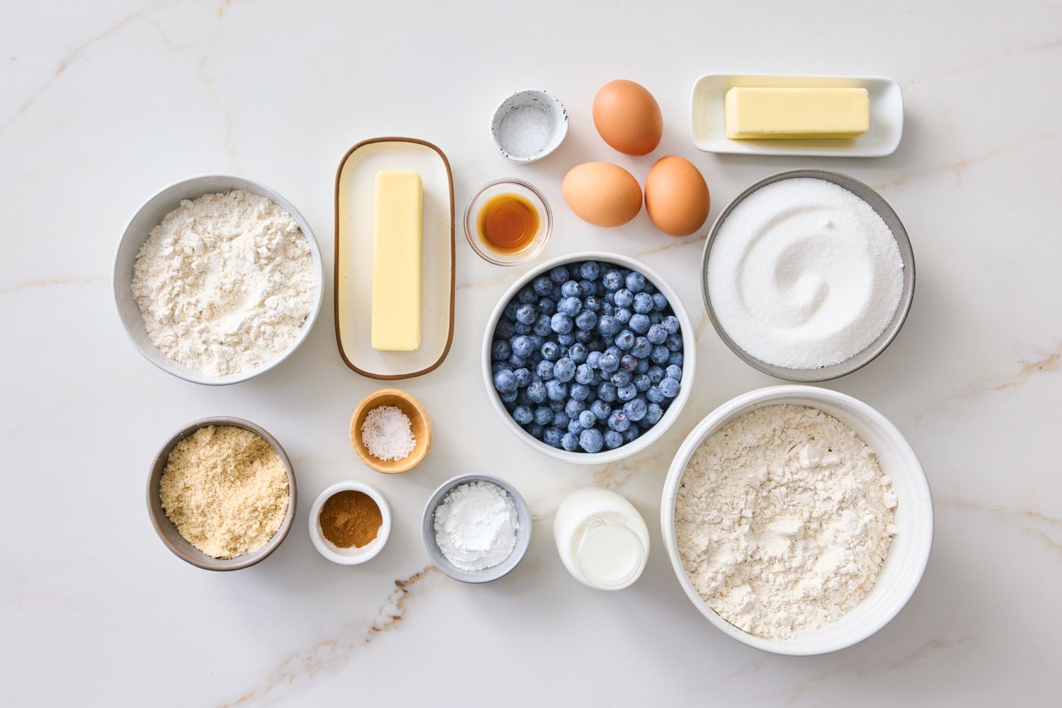 Ingredients arranged for making blueberry muffins including eggs flour sugar milk blueberries butter and baking essentials