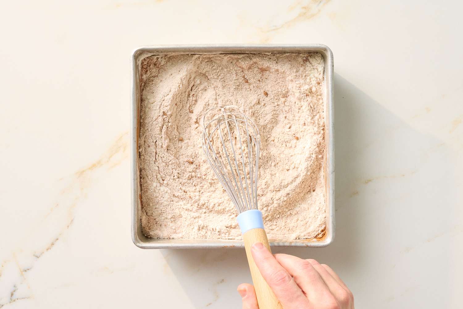A whisk in a mixed dry ingredient bowl for baking a hand holding the whisk